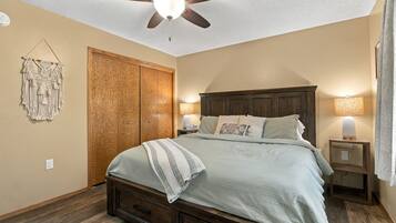 Une chambre à coucher comprenant un lit, un ventilateur de plafond, une armoire et une table de chevet avec une lampe.