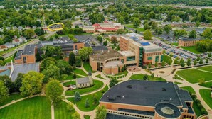 Vista aérea de um campus com vários edifícios, gramados verdes e um estacionamento.