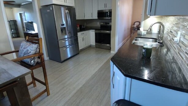 A modern kitchen with stainless steel appliances, white cabinets, and a black countertop. - Rancher's Capitol Lodge (Historic) - Steps away from the Capitol and Downtown (Cheyenne)