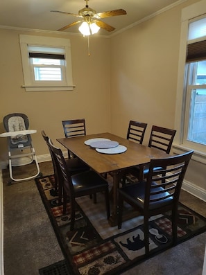 A dining area with a wooden table and six chairs, a ceiling fan, and a window with blinds.