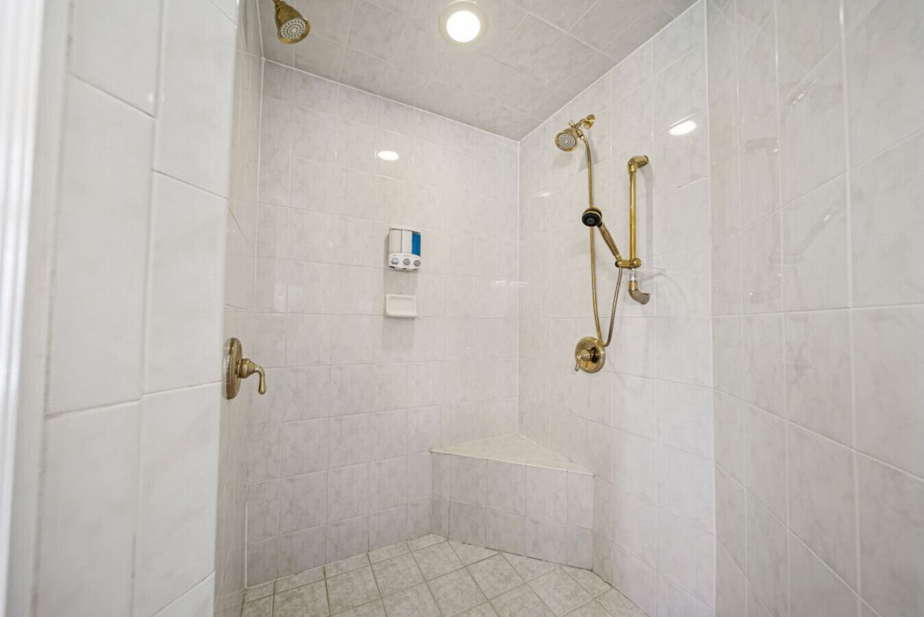 Une douche équipée d’un pommeau de douche à main, d’un robinet mural et d’un distributeur de savon.