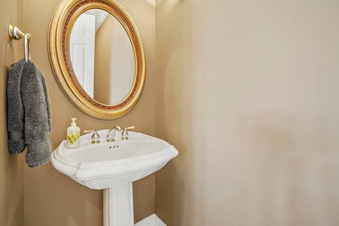 A bathroom with a white pedestal sink, a gold-framed mirror, and a towel rack with two towels.