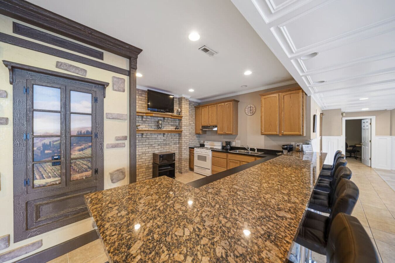 A kitchen with granite countertops, wooden cabinets, a brick wall, and a large island with seating.