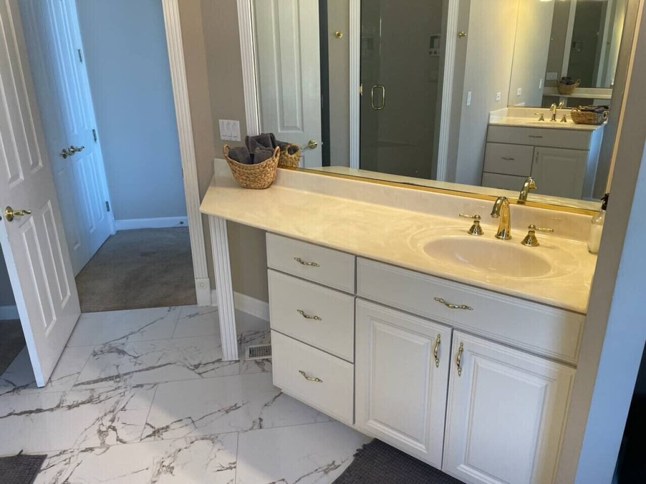 A bathroom with a marble floor, white cabinetry, a large mirror, and a double sink.