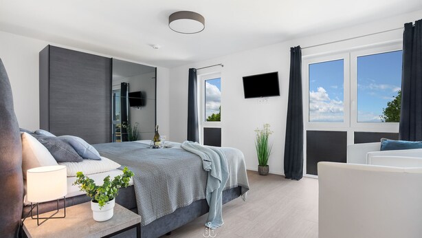 Et moderne soveværelse med seng, natbord, lampe og en potteplante.