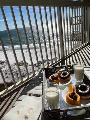 A beach view from a balcony with a tray of donuts and milk.