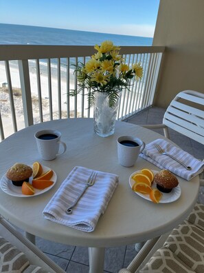 A round table with two white mugs, a white plate with a muffin and orange slices, a white plate with a muffin and orange slices, a white napkin with a fork, and a vase with yellow flowers. - RIGHT ON THE SUGAR, WHITE, SAND BEACH!! #1112 AWESOME VIEW! (Destin)
