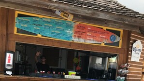 A bar with a wooden counter, colorful stools, and a menu board.