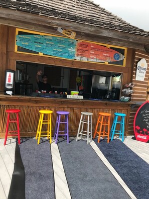 Eine Bar mit Holztresen, bunten Hocker und einer Speisekarte.