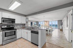 A modern kitchen with stainless steel appliances, white cabinetry, and a large island with a sink.