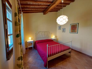 A bedroom with a bed, two bedside tables, a hanging light fixture, and a window with curtains.