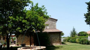 A stone well with a metal arch, a stone building with a tiled roof, and a well-maintained lawn. - Lovely flat with private covered terrace, pool, large shared garden. (Toscana)