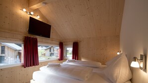Quarto de cabana de madeira com duas camas, uma TV na parede e janelas com cortinas.