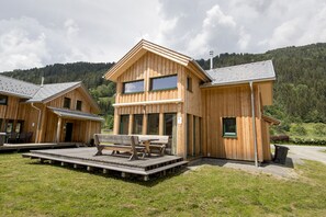 Eine Holzhütte mit einer Terrasse und Sitzgelegenheiten im Freien, umgeben von einem bewaldeten Hügelhang.