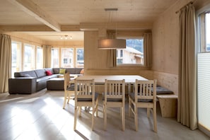 Ein Holzinnenraum mit Esstisch, Stühlen, einer Couch und großen Fenstern.