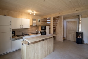 Eine moderne Küche mit Holzschränken, einer zentralen Kochinsel, Edelstahlgeräten und einem Kaminofen.