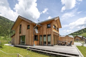 Une cabane en bois dotée d’une terrasse, de grandes fenêtres et surplombant un paysage montagneux.