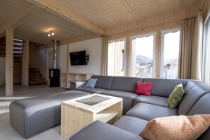 Ein modernes Wohnzimmer mit einem Ecksofa, einem Holztisch und einem an der Wand befestigten Fernseher.