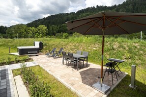 An outdoor patio with a hot tub, lounge chairs, and a table with an umbrella. - Murau 11 - large terrace & good location (Murau)