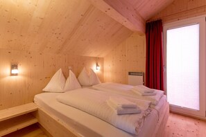 Une pièce de cabane en bois comprenant un lit, des oreillers et une fenêtre avec des rideaux.