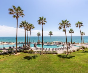 A resort with multiple swimming pools, palm trees, and a view of the ocean.