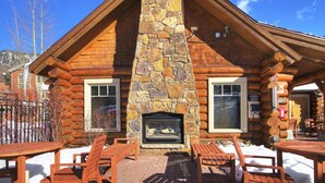 Une cabane en rondins avec une cheminée en pierre, une terrasse en bois et un espace salon extérieur.