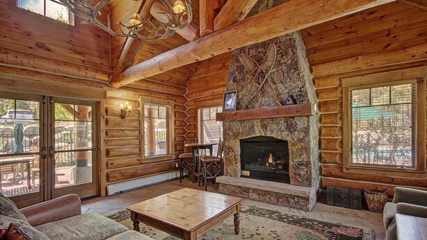 L’intérieur d’une cabane en rondins, avec une cheminée en pierre, des meubles en bois et de grandes fenêtres.