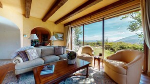 A cozy living room with a sofa, armchairs, and a coffee table. There is a large window offering a scenic view of the outdoors.