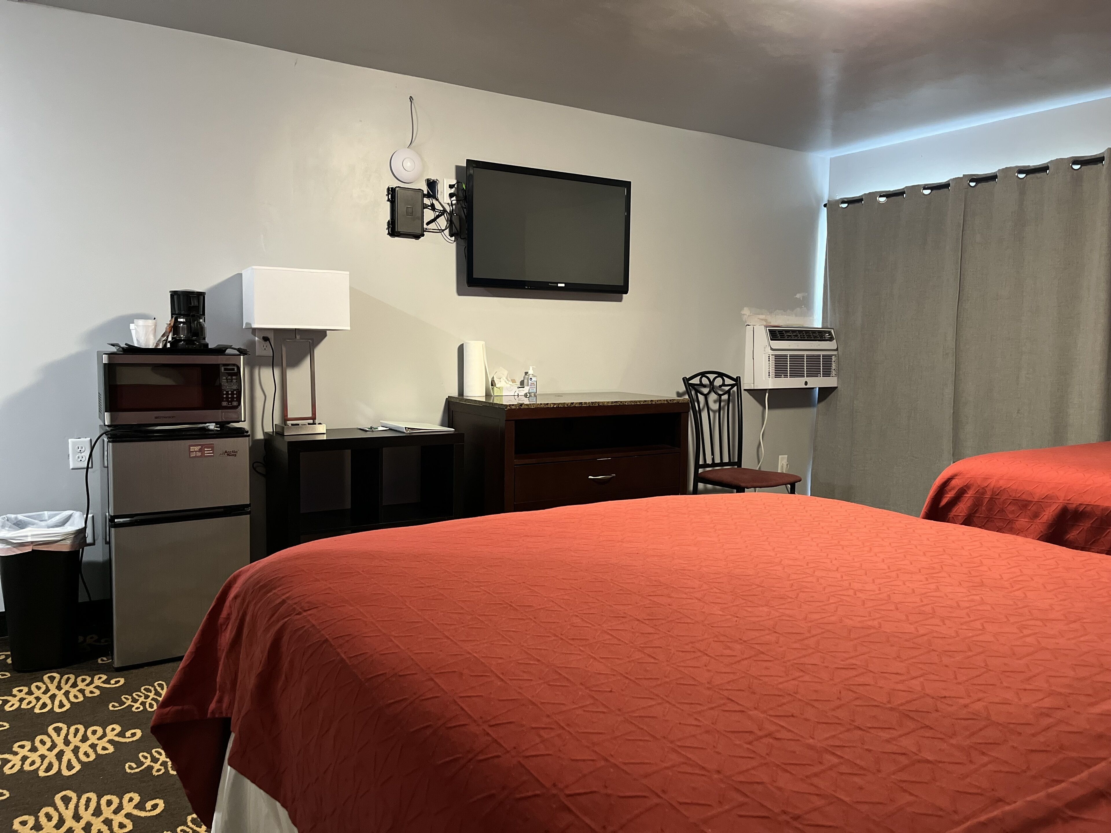 Habitación de hotel con dos camas, un escritorio con computadora, microondas, refrigerador, una silla, televisor de pantalla plana y aire acondicionado.