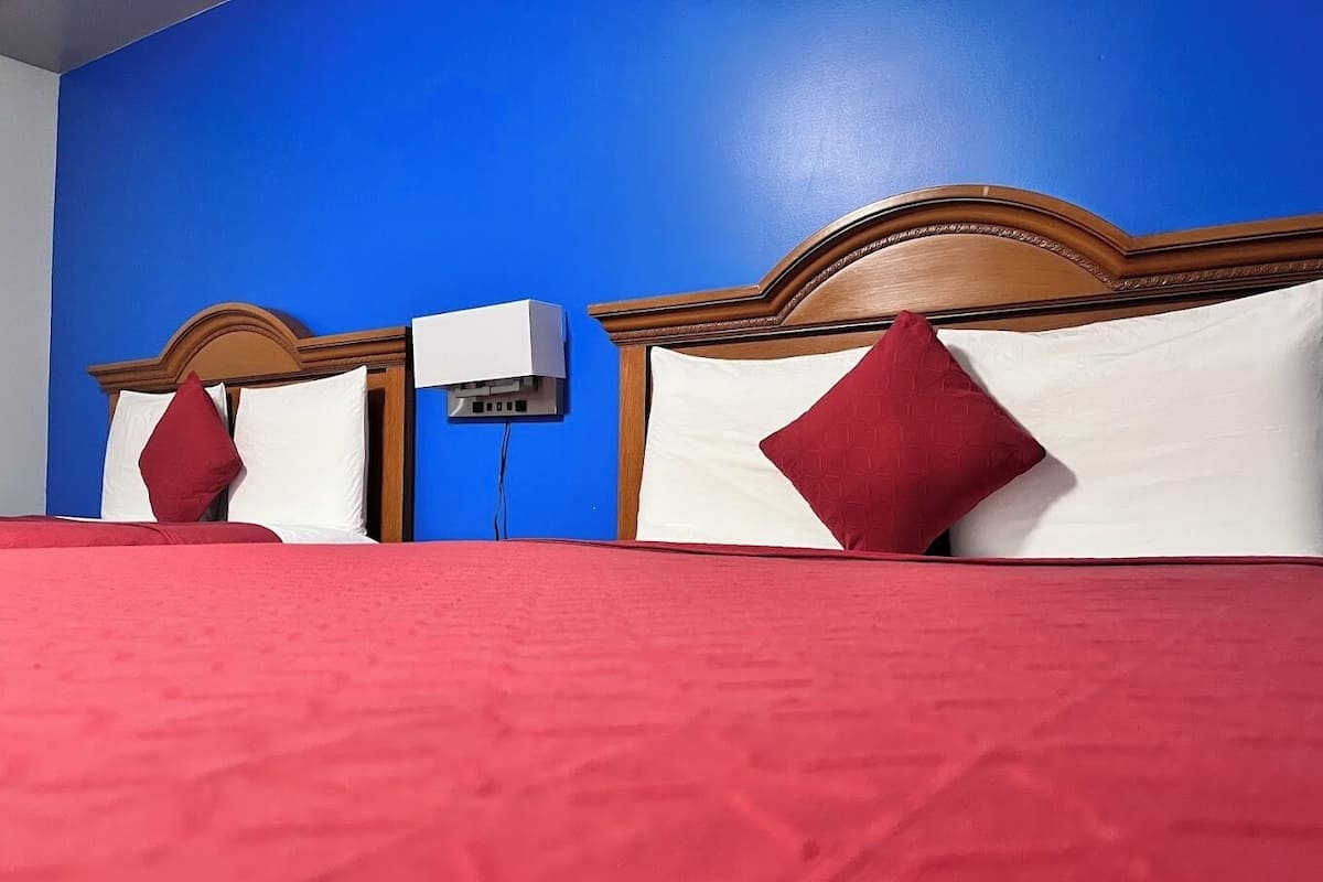Quarto de hotel com colcha vermelha, duas almofadas brancas e uma almofada decorativa vermelha.