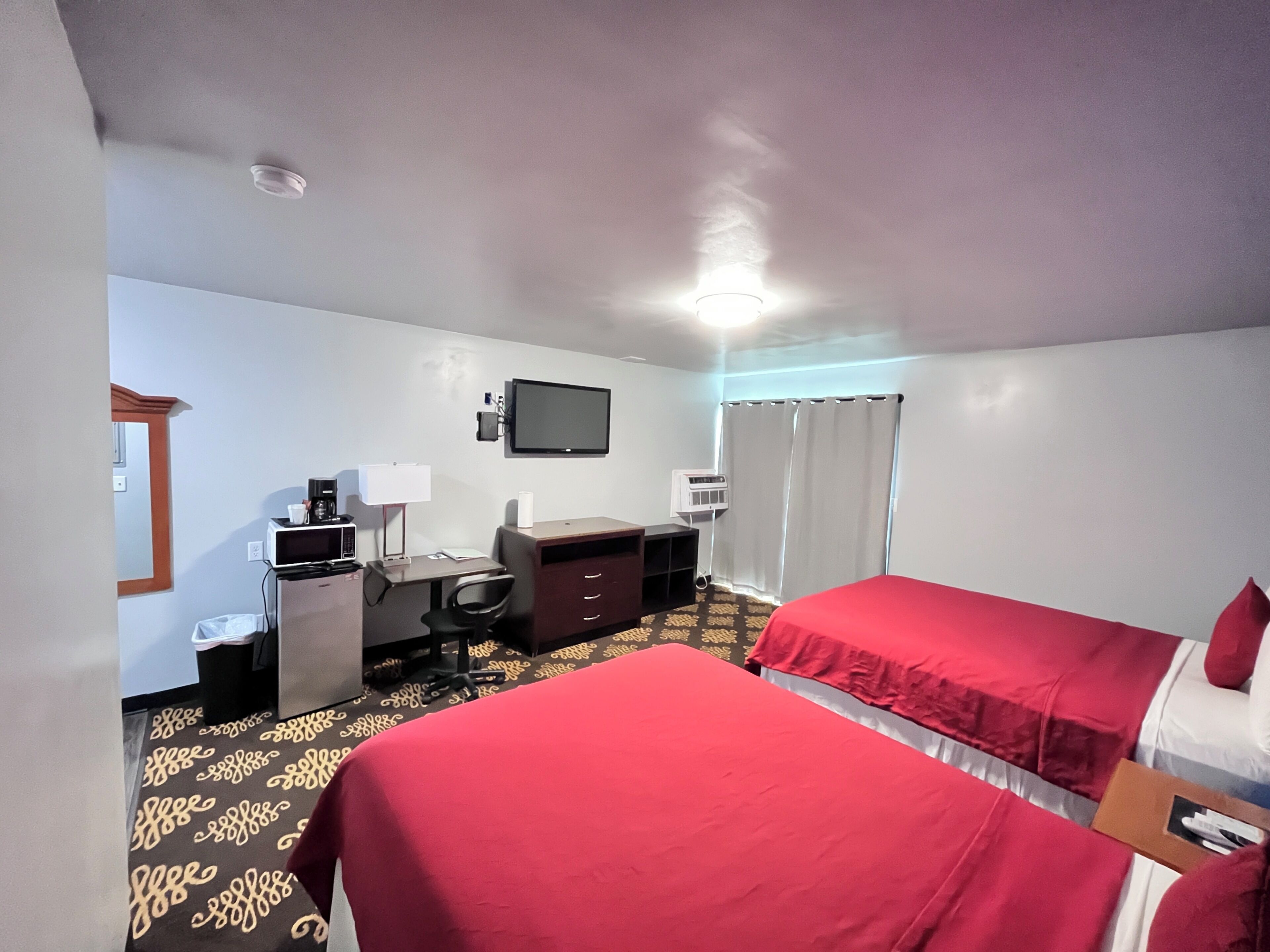 Ein Hotelzimmer mit zwei Betten, einem Schreibtisch, einem Sessel, einem Fernseher und einem Fenster mit Vorhängen.