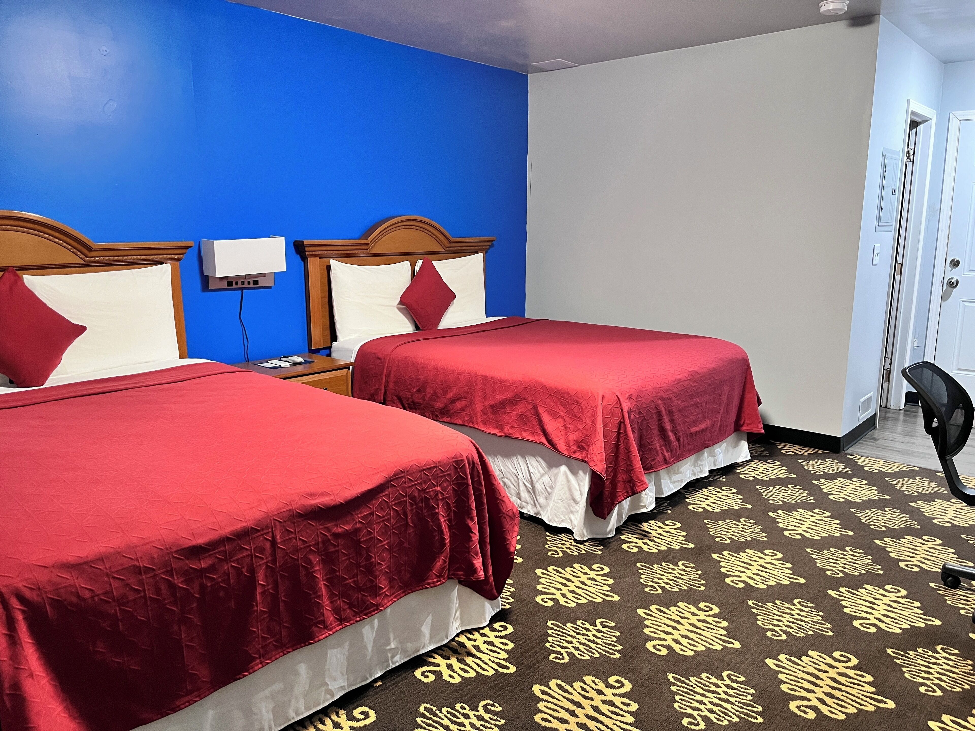 Habitación de hotel con dos camas, una pared azul y una alfombra estampada.