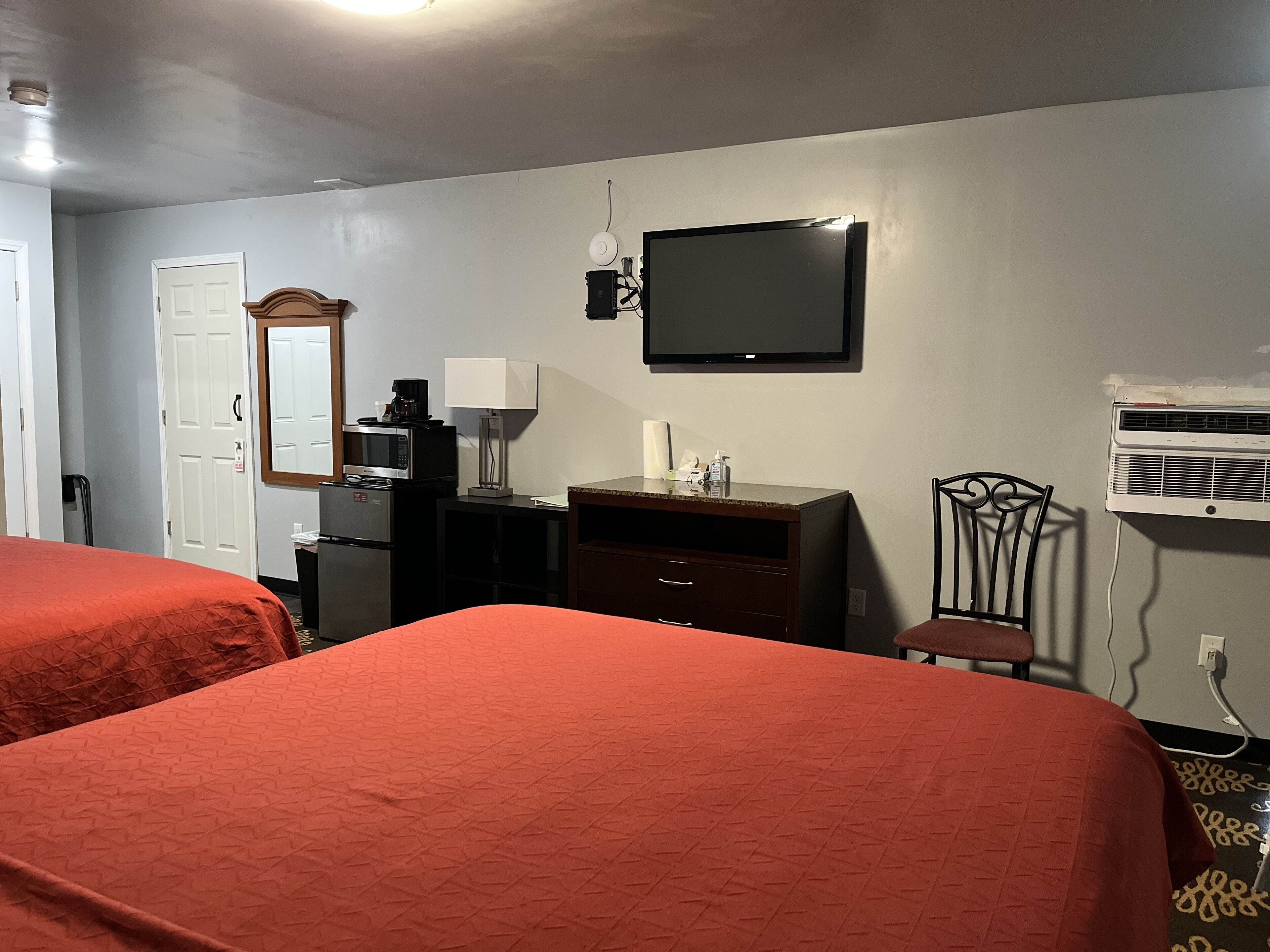Habitación de hotel con dos camas, televisión, microondas, refrigerador, escritorio con lámpara, una silla y aire acondicionado.