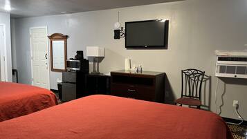 Habitación de hotel con dos camas, televisión, microondas, refrigerador, escritorio con lámpara, una silla y aire acondicionado.