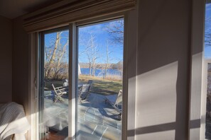 Ein Zimmer mit einer großen Schiebetür, die auf eine Terrasse mit Blick auf einen See und Bäume führt.