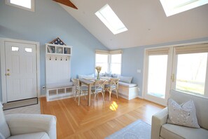 Ein Zimmer mit Holzboden, einer weißen Tür, einer weißen Bank, einem weißen Sofa und einem Tisch mit Stühlen.