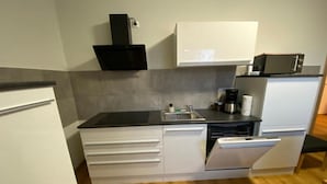 Cocina compacta con armarios blancos, una encimera negra, microondas y cafetera.