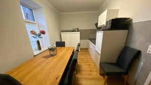 Una cocina compacta con una mesa de comedor de madera, sillas negras y un pequeño ventanal con flores.