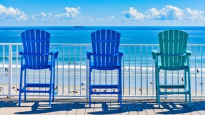 Drei Adirondack-Stühle auf einer Holzterrasse mit Blick auf einen Strand, einen klaren blauen Himmel und das Meer.