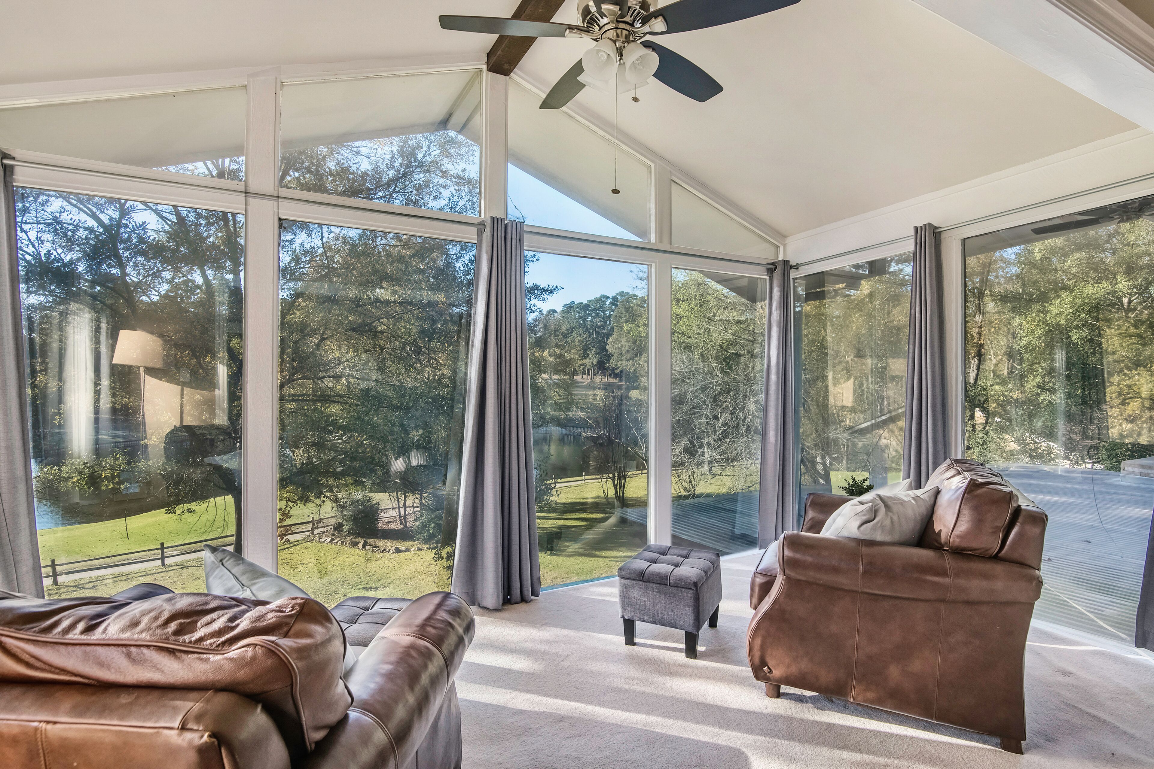 A spacious room with large windows, a ceiling fan, and a view of a green landscape.