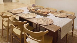 Un espace repas avec une longue table en bois, des sets de table en fibres tressées et des chaises en bois.