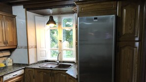 Eine Küche mit Holzausstattung, einem Edelstahlkühlschrank, einer Spüle und einem Fenster mit einer Pendelleuchte.