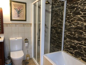 Een badkamer met toilet, een douche met glazen deur en een bad tegen een stenen muur.