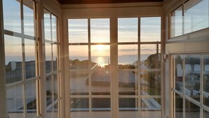 Parveke, jolta avautuu näkymä auringonlaskuun meren yllä, puiset kaiteet ja kirkas taivas.