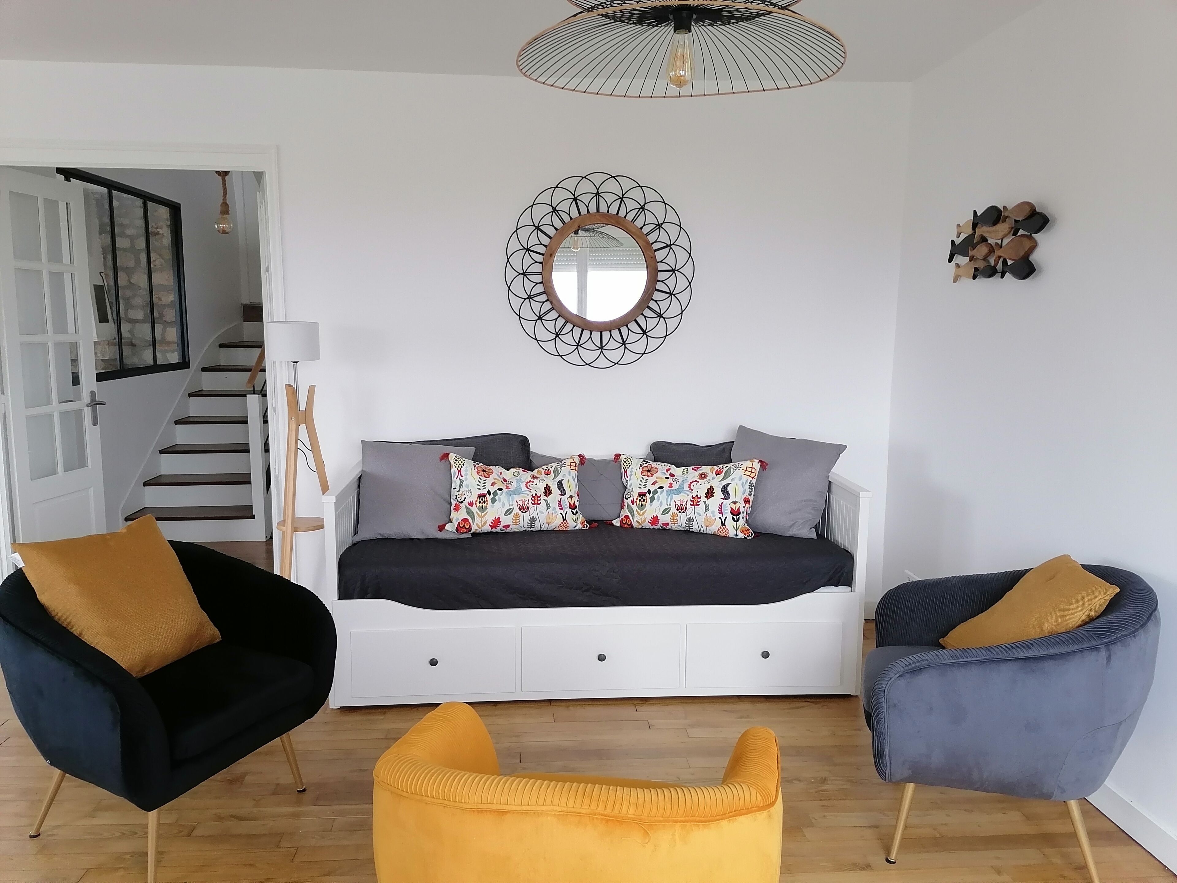 A modern living room with a sofa, two armchairs, a decorative mirror, and a hanging light fixture.