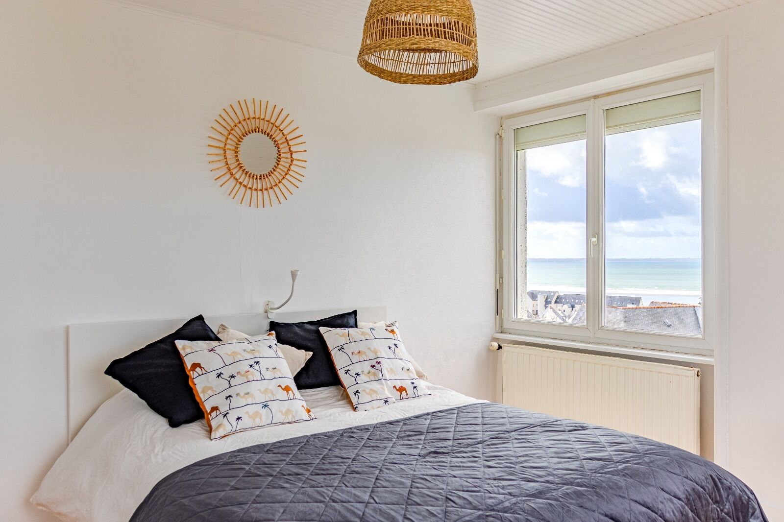 Une chambre avec un lit, une fenêtre donnant sur la mer et une décoration murale en forme de soleil.
