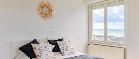 A bedroom with a bed, a window with a view of the sea, and a sun-shaped wall decoration.