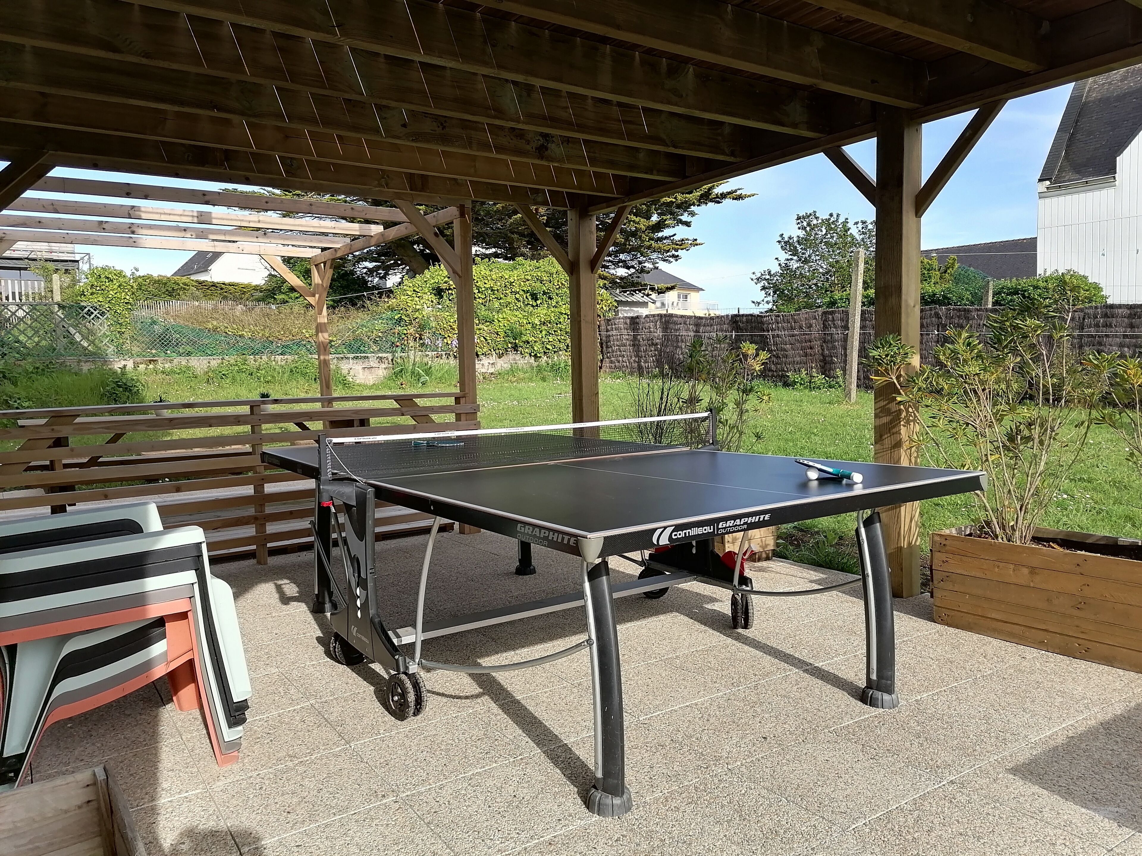 An outdoor table tennis table with a canopy, a bench, and a table with chairs.