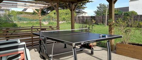 An outdoor table tennis table with a canopy, a bench, and a table with chairs.
