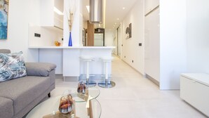 Un salón moderno con un sofá gris, una mesa de centro de cristal y dos taburetes blancos.